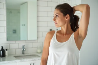 Femme examinant ses aisselles dans un miroir de salle de bain moderne, explorant des solutions d'épilation durables